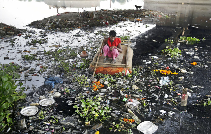 In this photo taken May 28, 2018, Ram Nath, 40, who makes a living from recycling trash, rummages for plastic bottles and other reusable trash while rowing a makeshift boat through murky waters of Yamuna, India's sacred river that flows through the capital of New Delhi. Photo: Altaf Qadri / Associated Press