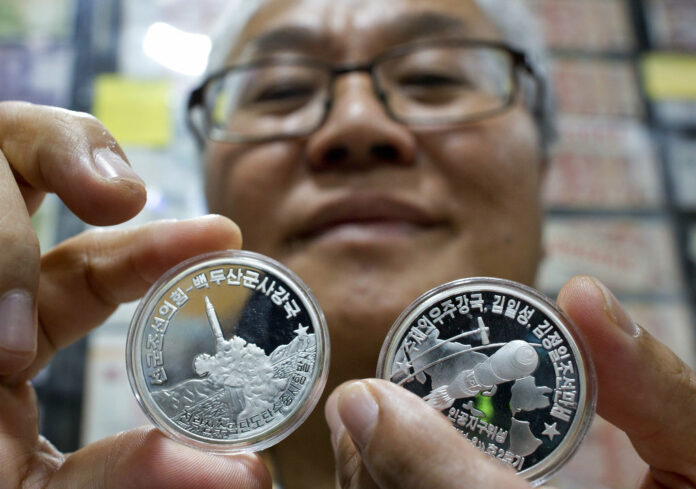 Rare coin dealer Joseph Poh on Monday displays two North Korean coins depicting its rockets program in Singapore. Photo: Gemunu Amarasinghe / Associated Press