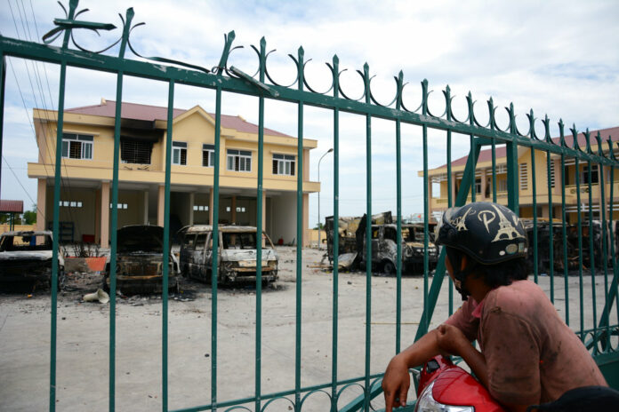 A motorist looks at charred vehicles burned by protesters at a fire and police station Tuesday in the south central province of Binh Thuan, Vietnam. Photo: Associated Press