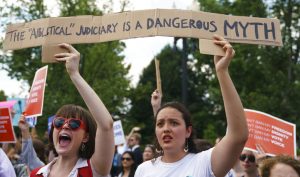 Protesters hold up a sign that reads "The Apolitical Judiciary Is A Dangerous Myth" against the Supreme Court ruling upholding President Donald Trump's travel ban . Photo : Carolyn Kaster / Associated Press