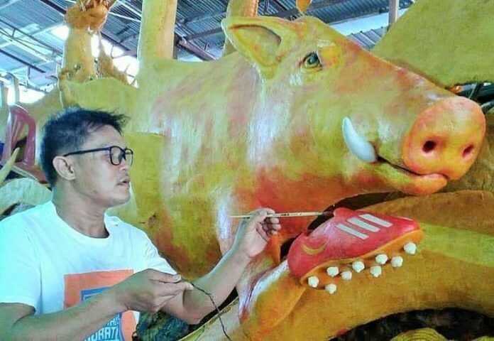 Sculptor Thien Leisrisip paints a a wax carved wild boar’s red Adidas football boots.