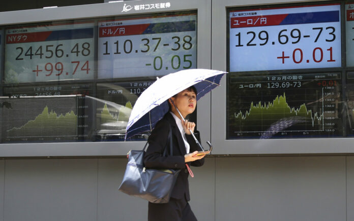 A woman walks by an electronic stock board of a securities firm in July in Tokyo, Japan. Photo: Koji Sasahara / Associated Press