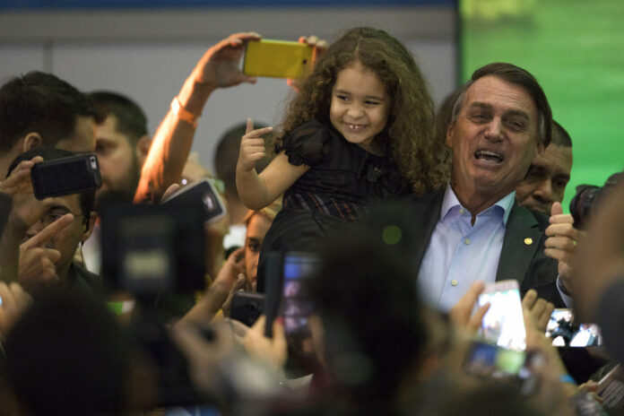 Presidential candidate Jair Bolsonaro holds a little girl as he poses for photos with supporters during the National Social Liberal Party convention where he accepted the party's nomination in July in Rio de Janeiro, Brazil. Photo: Leo Correa / Associated Press
