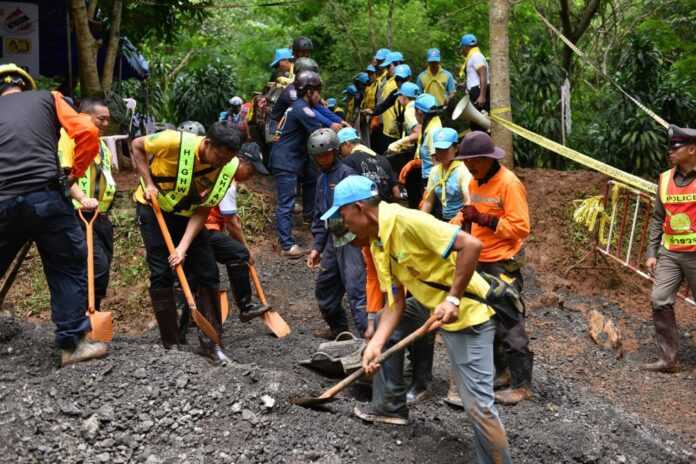 Volunteers help public workers put sand and dry soil Sunday on top of the muddy road leading to Luang Khun Nam Nang Non cave in Chiang Rai province.