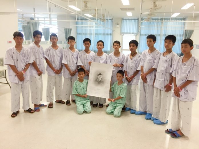 Twelve boys and their football coach pose for a photo with a drawing of Lt. Cmdr. Saman Kunan, Sunday at Chiangrai Prachanukroh Hospital.