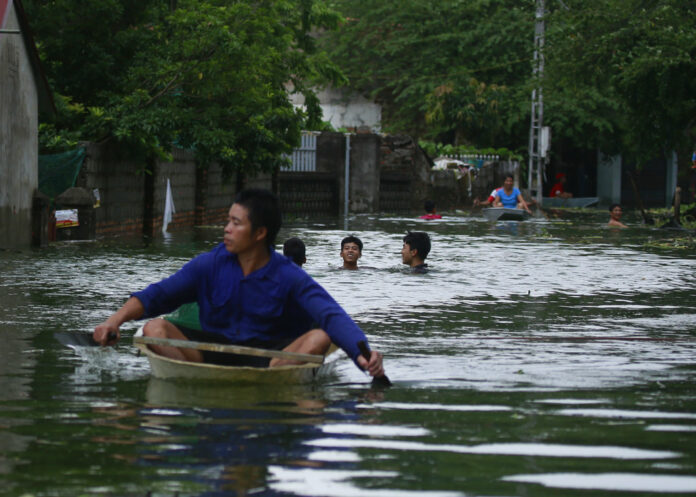 A man paddles a boat and others swim through flooded villageon July 31, 2018 in Chuong My district, Hanoi, Vietnam. Photo: Manh Thang/ Associated Press File