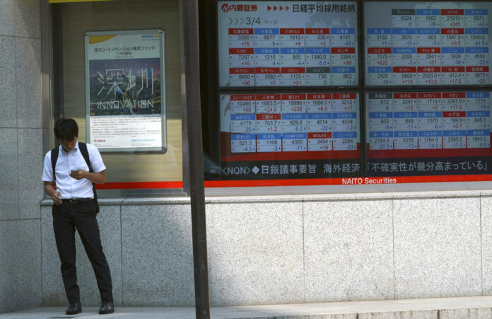 A man stands near an electronic stock board showing Japan's Nikkei 225 index and other countries indexes at a securities firm in Tokyo Friday, Aug. 3, 2018. Photo: Eugene Hoshiko/ Associated Press