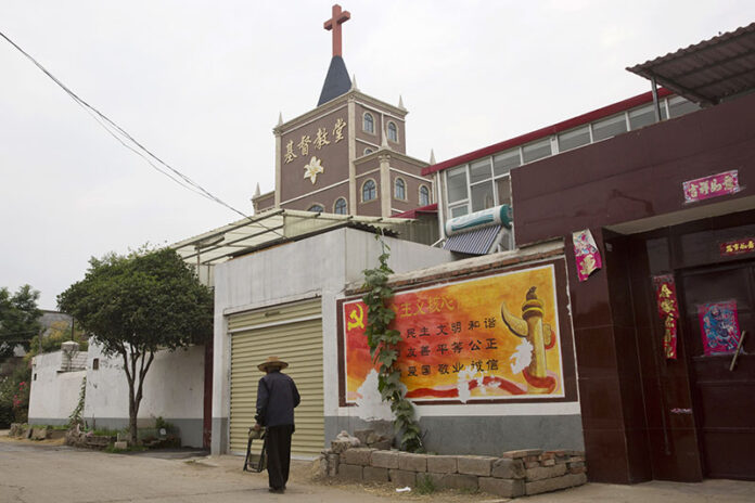 In this photo taken Saturday, June 2, 2018, a resident walks past a government billboard citing core values of the Communist Party near a church in the city of Pingdingshan in central China's Henan province. Photo: Ng Han Guan / Associated Press