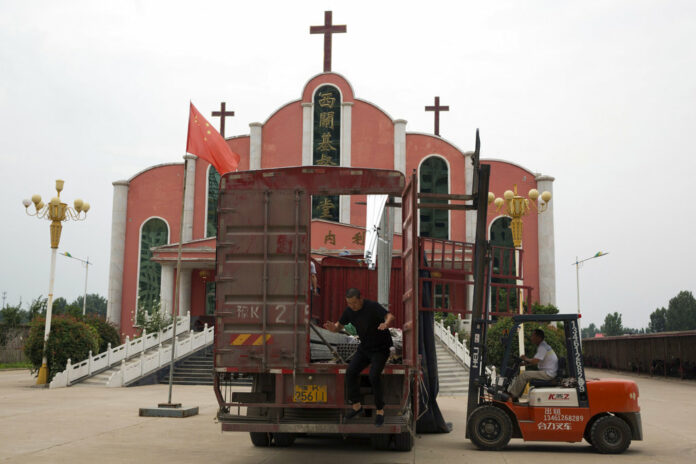 A worker jumps from a truck parked in front of a church and the Chinese national flag in June near the city of Pingdingshan in central China's Henan province. Photo: Ng Han Guan / Associated Press