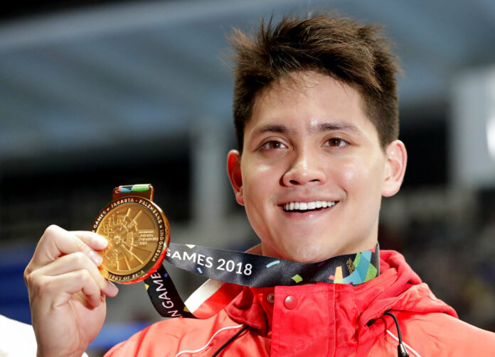 Singapore's Joseph Schooling holds up his gold medal up for photographers after winning the men's 100m butterfly final Wednesday during the swimming competition at the 18th Asian Games in Jakarta, Indonesia. Photo: Lee Jin-man / Associated Press