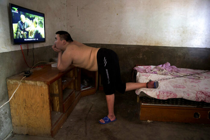 In this July 12, 2018, photo, Li Mingming, whose foot is chained to a bed, a practice sometimes employed by families in rural China to keep mentally disabled relatives from wandering away, watches television in this home in Gucheng village in central China's Henan province. Photo: Ng Han Guan / Associated Press