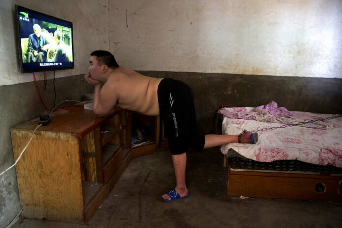 In this July 12, 2018, photo, Li Mingming, whose foot is chained to a bed, a practice sometimes employed by families in rural China to keep mentally disabled relatives from wandering away, watches television in this home in Gucheng village in central China's Henan province. Photo: Ng Han Guan / Associated Press In this July 12, 2018, photo, Li Mingming, whose foot is chained to a bed, a practice sometimes employed by families in rural China to keep mentally disabled relatives from wandering away, watches television in this home in Gucheng village in central China's Henan province. Photo: Ng Han Guan / Associated Press