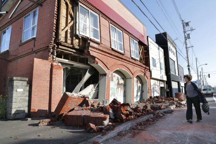 A woman walks past a damaged building Thursday in Abira town, near Chitose, Hokkaido, northern Japan. Photo: Masanori Takei / Associated Press