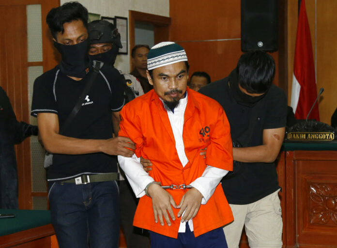Islamic militant Wawan Kurniawan, center, is escorted by masked police officers upon arrival for his Thursday trial at West Jakarta District Court in Jakarta, Indonesia. Photo: Tatan Syuflana / Associated Press