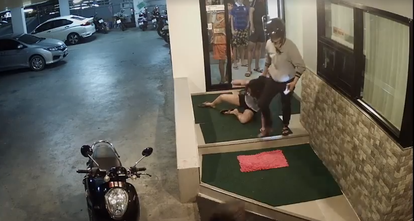 A woman is beaten by her girlfriend in a Bangkok parking lot while several people look on in a still image from a security camera. Image: Thikampron Kaain / Facebook
