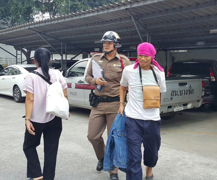 A police officer Tuesday leads away a man accused of stabbing a German man near BTS Mo Chit.