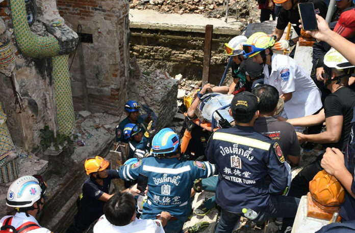Rescue personnel lift an injured worker Tuesday from the debris of a collapsed temple bell tower in west Bangkok.