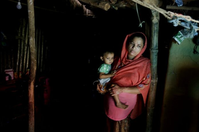 Rohingya refugee woman Minara Begum, mother of Rahima Akter, holds her youngest daughter Arohi Zannat inside the family hut in August in Kutupalong refugee camp, Bangladesh. Photo: Altaf Qadri / Associated Press