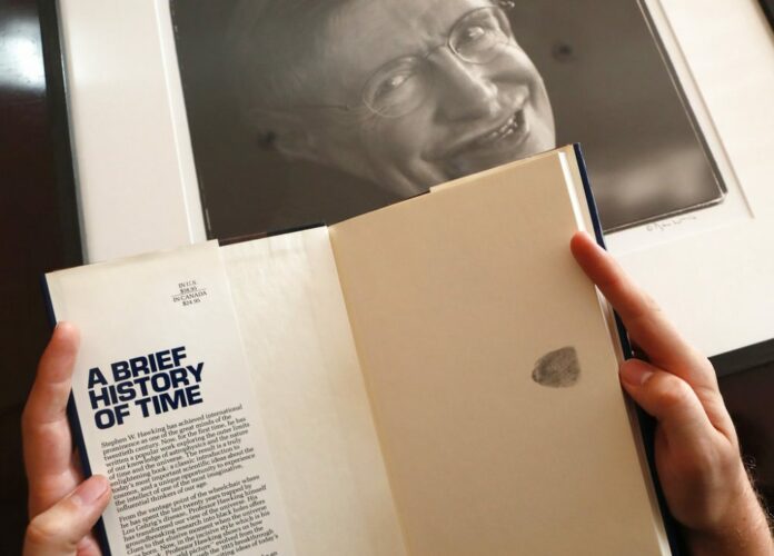 A Book, signed with a thumb print by Stephen Hawking is one of the personal and academic possessions of Stephen Hawking, photo behind, at the auction house Christies in London, Friday, Oct. 19, 2018. Photo: Frank Augstein / Associated Press