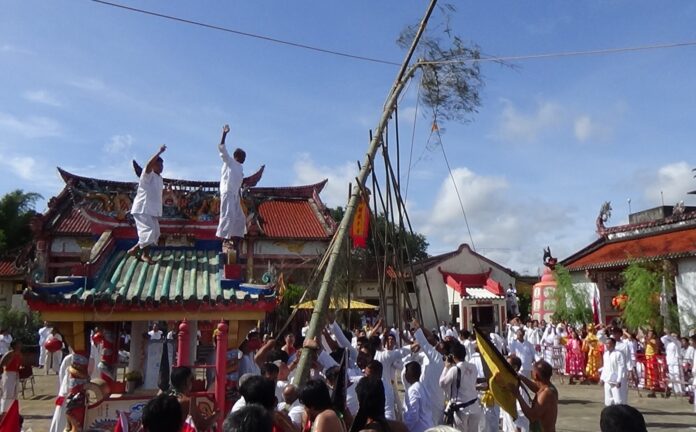Believers raise a sacred pole Monday to connect earth with heaven at a shrine in Trang province.