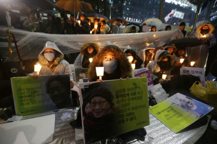 College students hold portraits of the deceased former South Korean sex slaves who were forced to serve for the Japanese military in World War II, and lit candles during a rally against Japanese government in front of the Japanese Embassy in Seoul, South Korea. Photo: Ahn Young-joon / Associated Press
