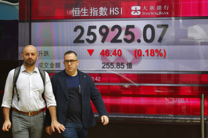 Two men walk past an electronic board showing Hong Kong share index outside a bank Thursday in Hong Kong. Photo: Kin Cheung / Associated Press