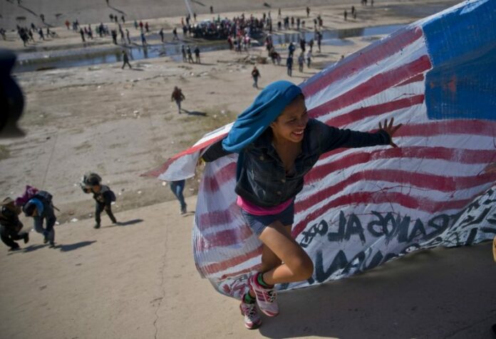 A migrant woman on Sunday helps carry a handmade U.S. flag up the riverbank at the Mexico-U.S. border after getting past Mexican police at the Chaparral border crossing in Tijuana, Mexico. Photo: Ramon Espinosa / Associated Press