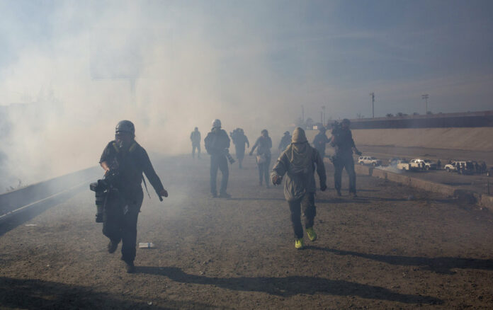 Migrants run from tear gas launched by U.S. agents, amid photojournalists covering the Mexico-U.S. border, after a group of migrants got past Mexican police at the Chaparral crossing Sunday in Tijuana, Mexico. Photo: Rodrigo Abd / Associated Press