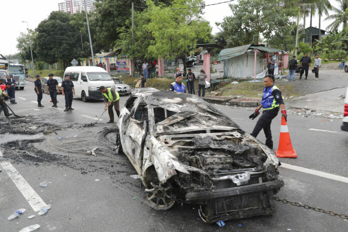 Police remove the wreckage of a burned car Tuesday after rioting outside Sri Maha Mariamman temple in Subang, Malaysia. Photo: Vincent Thian / Associated Press