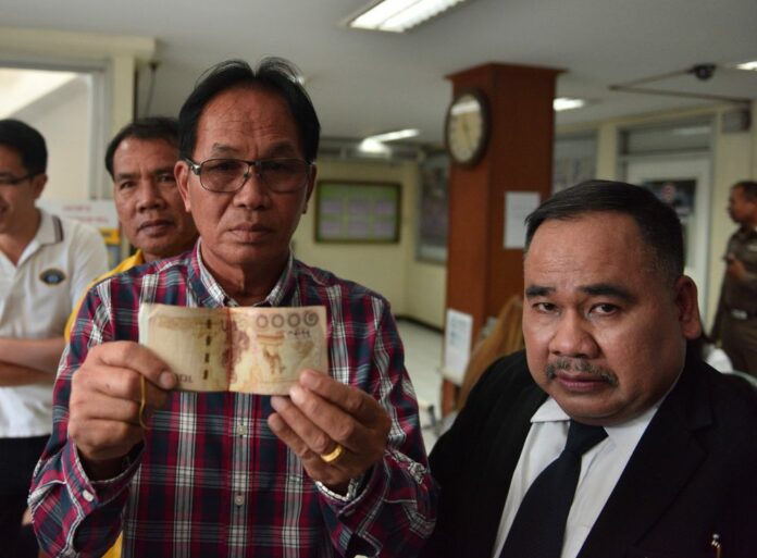 Boonlert Kanpakdee holds 100,000 baht with attorney Songkran Atchariyasap, at right, Monday at Khan Na Yao Police Station.