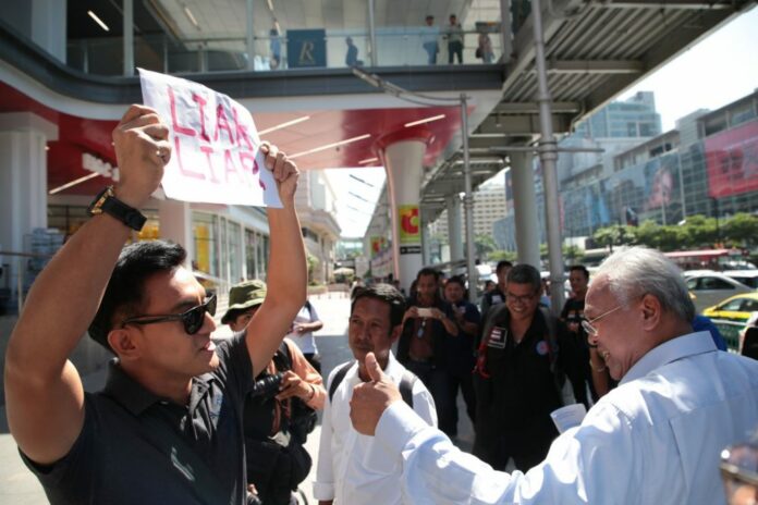 Akawutt 'Ake' Auttagorn holds a sign reading 'Liar Liar' as Suthep Thaugsuban canvasses Wednesday at Big C Ratchadamri.