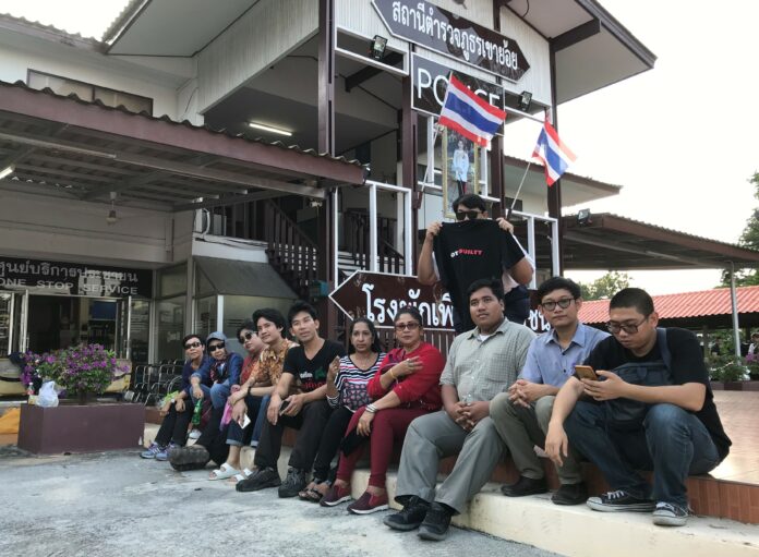 Sirawith “Ja New” Seritiwat, third from right, sits with his supporters Sunday in front of Khao Yoi police station in Phetchaburi province.