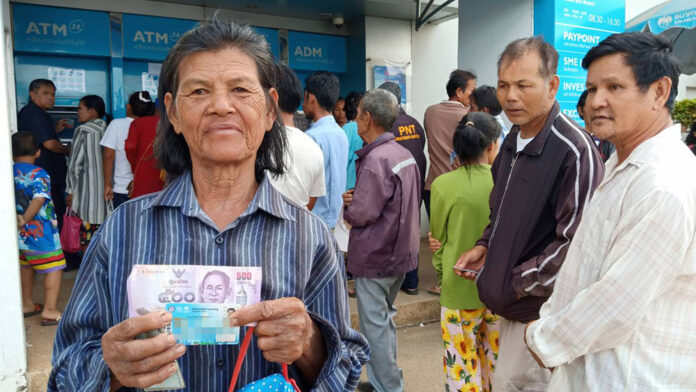 A welfare card holder shows a 500-baht note Wednesday in front of Krung Thai ATMs in Prachin Buri province.