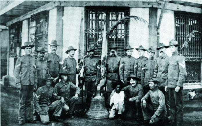 U.S. soldiers of Company C, 9th Infantry Regiment who survived a Filipino ambush in 1901 pose with a church bell used to signal the attack. Photo: Fred R. Brown / Wikimedia Commons