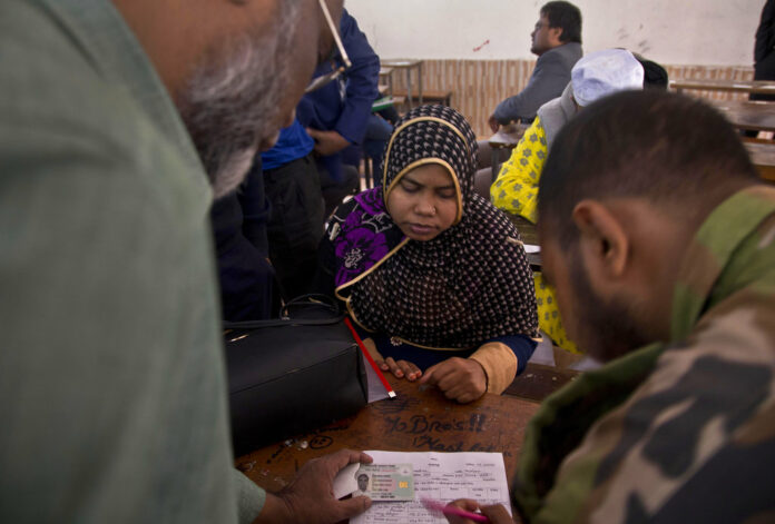 Bangladeshi election officials help a woman to find name of her family member in the voters list at a polling station ahead of the general elections Thursday in Dhaka, Bangladesh. Photo: Anupam Nath / Associated Press