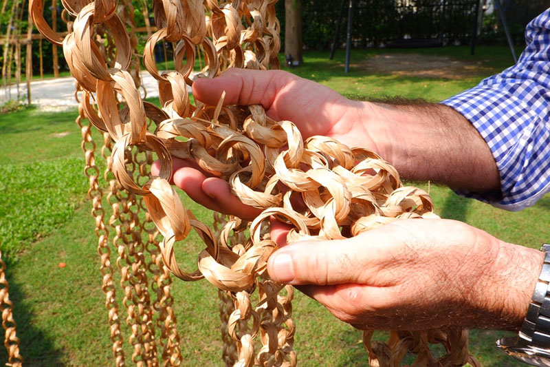 Popovic holds up hanging chains of dried grass, part of a playground installation.