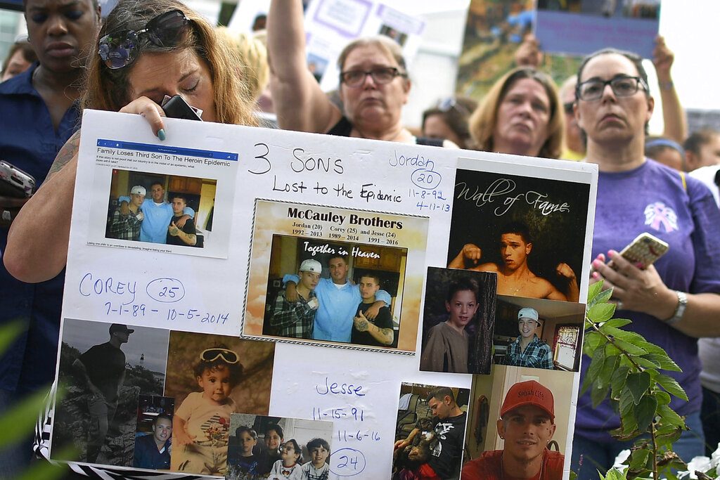 Jeanmarie McCauley, left, of Rockland, Massachusetts, rests her head on a sign she made of her three children who died within three years to drug addiction, as family and friends who lost loved ones to OxyContin and opioid overdoses stage a protest outside the headquarters of Purdue Pharma in August in Stamford, Connecticut. Photo: Jessica Hill / Associated Press