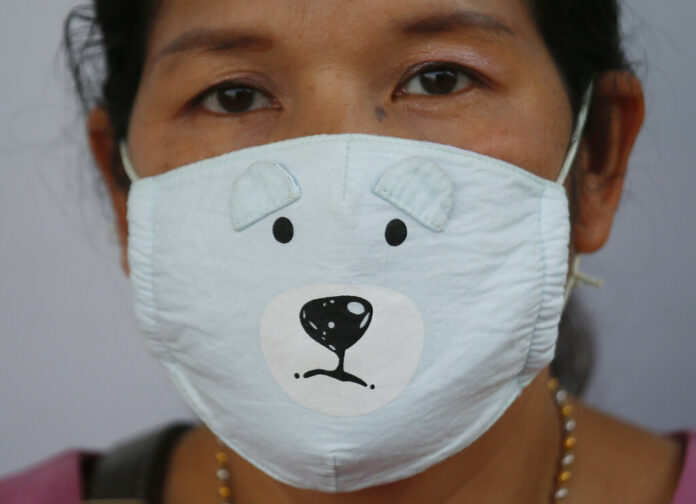 A woman on Monday wears a protective mask while waiting for a bus during smoggy conditions in Bangkok. Photo: Sakchai Lalit / Associated Press
