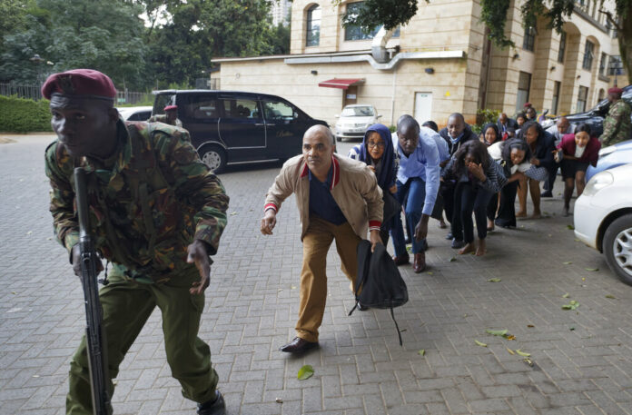 Civilians who had been hiding in buildings flee under the direction of a member of security forces at a hotel complex in Nairobi, Kenya. Photo: Ben Curtis / Associated Press