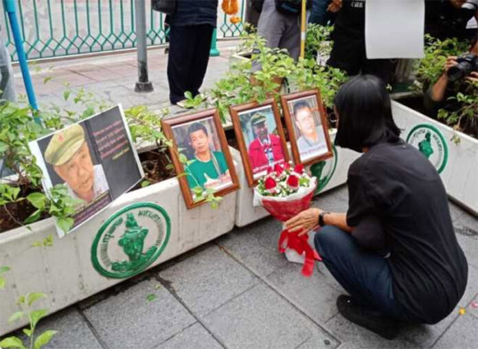 A mourner lays flower at a commemoration event Feb. 2 in Bangkok for missing activist Surachai Danwattananusorn, pictured in the center, and two of his aides whose bodies were found in the Mekong River.