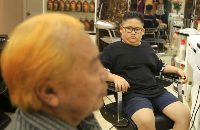 Le Phuc Hai, 66, at left, and To Gia Huy, 9, sit after having Trump and Kim haircuts Tuesday in Hanoi. Photo: Hau Dinh / Associated Press