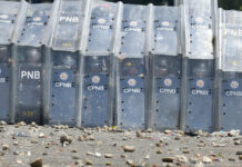 Venezuela Standoff Turns Deadly as Troops Block Aid Delivery Officers of the Venezuela's Bolivarian National Police take cover behind their shields from a shower of rocks as they block the Simon Bolivar International Bridge on Saturday in La Parada near Cucuta, Colombia. Photo: Fernando Vergara / Associated Press
