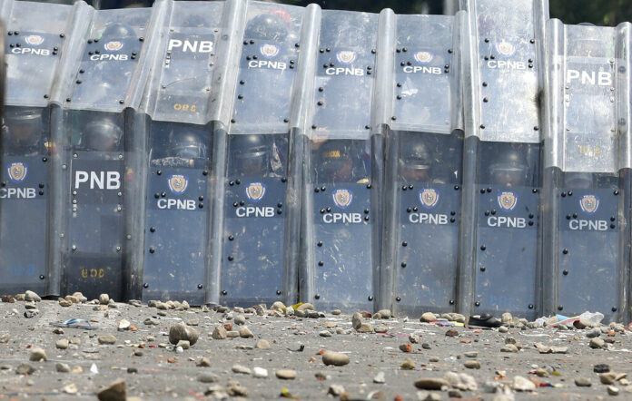 Officers of the Venezuela's Bolivarian National Police take cover behind their shields from a shower of rocks as they block the Simon Bolivar International Bridge on Saturday in La Parada near Cucuta, Colombia. Photo: Fernando Vergara / Associated Press