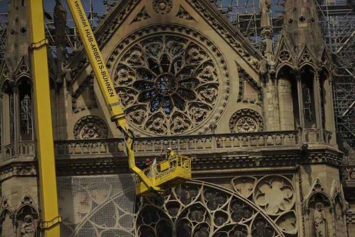 Workers fix a net to cover one of the iconic stained glass windows of the Notre Dame Cathedral in Paris, Sunday, April 21, 2019. (AP Photo/Francisco Seco)