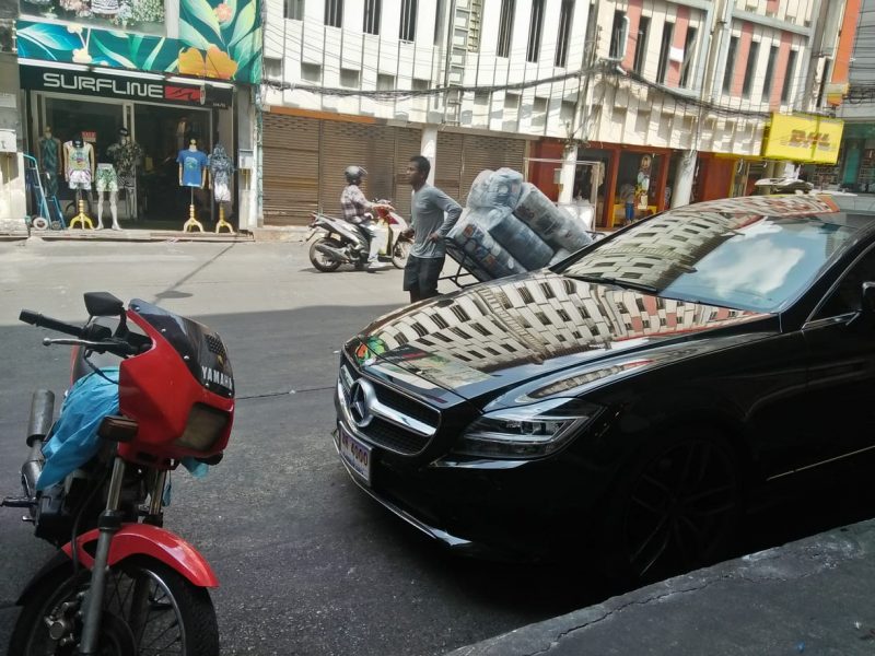 A street vendor carrying a load of goods passes a late-model Mercedes-Benz. Thor. Photo: Ben Bartee