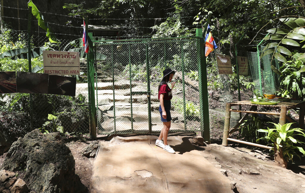 In this Saturday, June 22, 2019, photo, a tourist stands at the gate the Tham Luang Nang Non cave in Mae Sai, Chiang Rai province, in northern Thailand. Some of the 12 young Thai soccer players and their coach have marked the anniversary of their ordeal that saw them trapped in a flooded cave for two weeks with a commemorative marathon in northern Thailand. Photo: Sakchai Lalit / AP