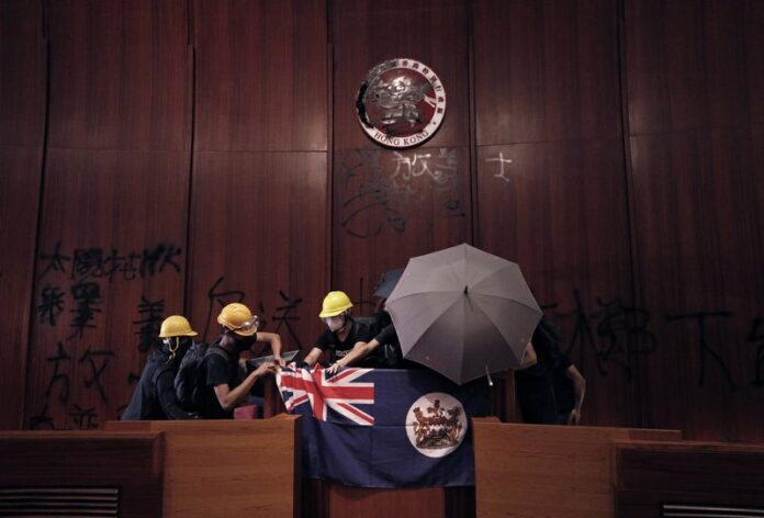 In this July 1, 2019, file photo, protesters put a Hong Kong colonial flag and deface the Hong Kong logo at the Legislative Chamber after they broke into the Legislative Council building in Hong Kong. (AP Photo/Vincent Yu, File)
