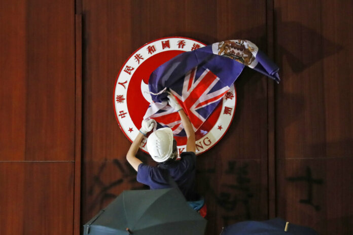 A protester covers the Hong Kong emblem with Hong Kong colonial flag after they broke into the Legislative Council building in Hong Kong, Monday, July 1, 2019. Protesters in Hong Kong took over the legislature's main building Monday night, tearing down portraits of legislative leaders and spray painting pro-democracy slogans on the walls of the main chamber. Photo: Kin Cheung / AP