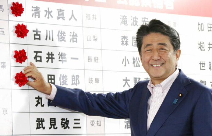 Japanese Prime Minister Shinzo Abe smiles in front of red rosettes on the names of his Liberal Democratic Party's winning candidates during ballot counting for the upper house elections at the party headquarters in Tokyo, Sunday, July 21, 2019. Prime Minister Abe's ruling coalition appeared certain to hold onto a majority in Japan's upper house of parliament, with exit polls from Sunday's election indicating he could even close in on the super-majority needed to propose constitutional revisions. Photo: Koji Sasahara / AP