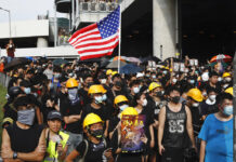 Hong Kong Police Tear Gas Protest Against Mob Violence Protesters hold up a poster with the words "Stop violence" and a U.S. flag as they face off with riot police at the entrance to a village at Yuen Long district in Hong Kong Saturday, July 27, 2019. Photo: Vincent Yu / AP